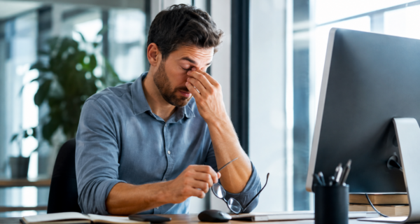 Office worker rubbing tired, dry eyes after prolonged screen use